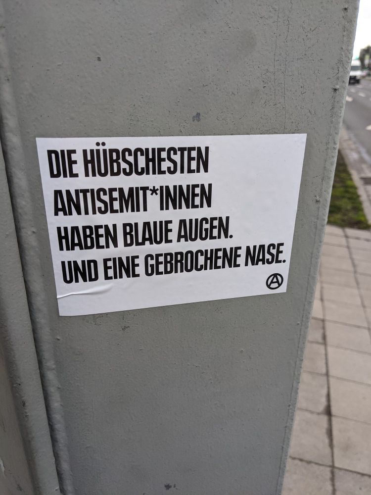 A sticker saying, in German: 
DIE HÜBSCHESTEN ANTISEMIT*INNEN HABEN BLAUE AUGEN. UND EINE GEBROCHENE NASE.