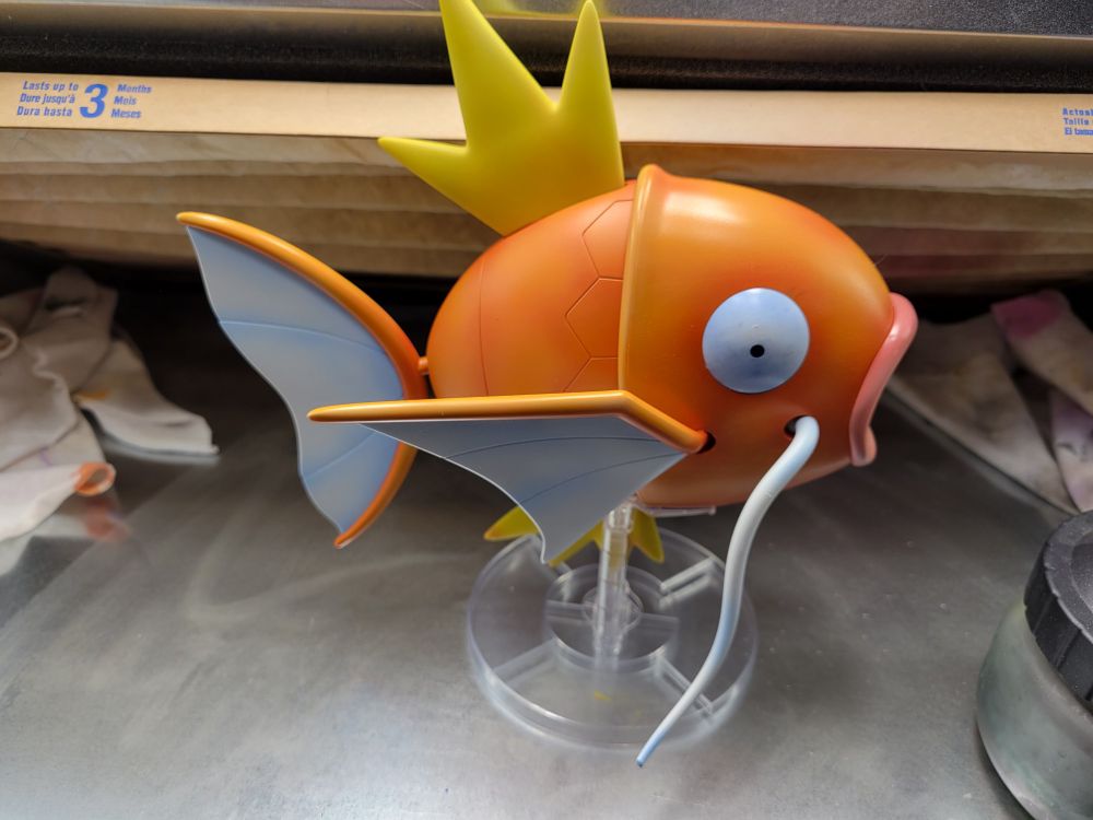 A magikarp model. It's female (It has shorter white whiskers). It's canon colors, but there's a subtle depth to them. Different parts of the fish have different surface finishes, the head is a high gloss, the body is a semi gloss. The whiskers are a matte white.

You can tell the white parts (eyes, fin webbing, whiskers) are shaded with blue. The scales on the body have darker orange where the scales all meet.