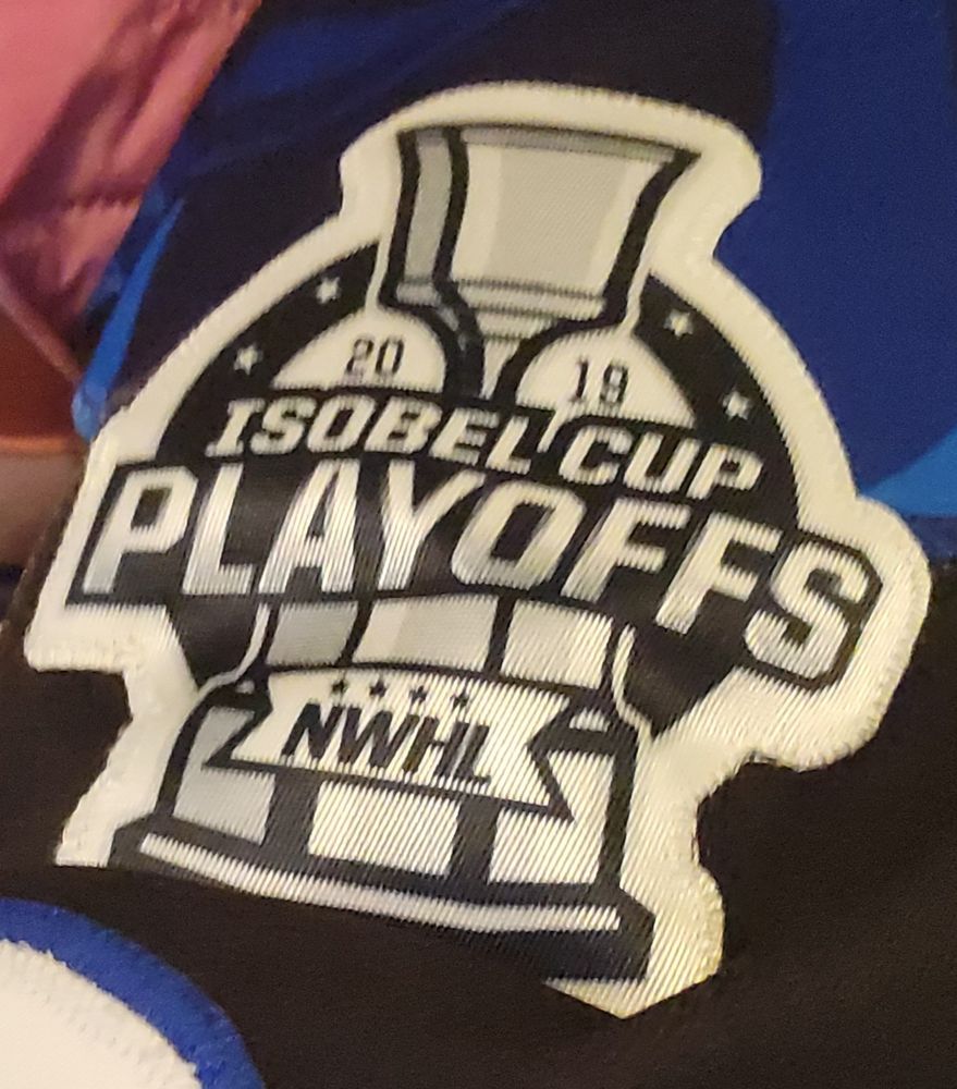 A hockey sweater patch of a silver trophy on a tiered base. It says Isobel Cup Playoffs 2019 above the NWHL logo. 