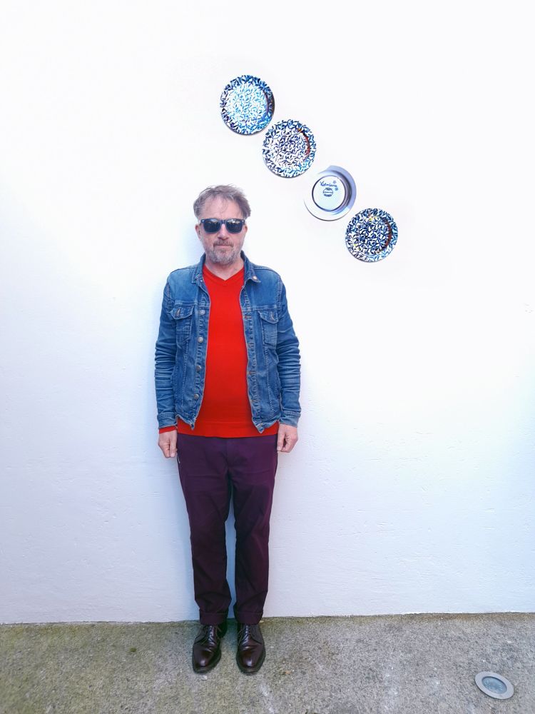 Micheál O'Connell with his new work 'Irish Broken English China' (4 plates arranged on the wall diagonally) at the opening of Uillinn: West Cork Arts Centre members and friends Exhibition 31st May 2025.
