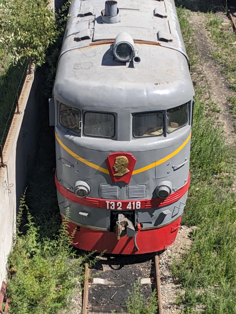 A close up shot of the front of an old diesel (I think) locomotive parked in a siding just to the east of Ulaanbaatar's central railway station. It's grey and red with a yellow lightning bolt stripe running around its front.