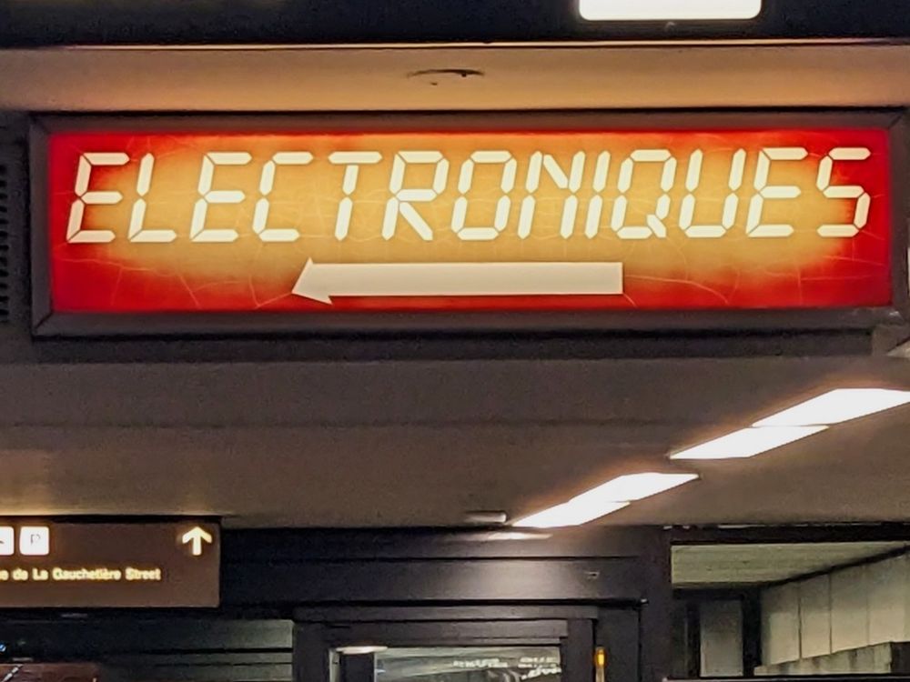 A somewhat faded sign with white type on a faded reddish orange background. The text reads "Electroniques" and is in classic pocket calculator font.