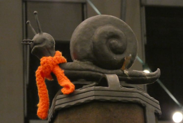 Eine Schneckenfigur mit einem orangefarbenen Schal um den Hals.