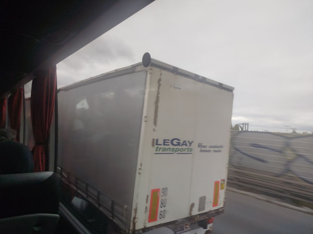 Photo prise depuis un bus. On peut voir un camion sur l'autoroute avec la mention "Le gay transports" 