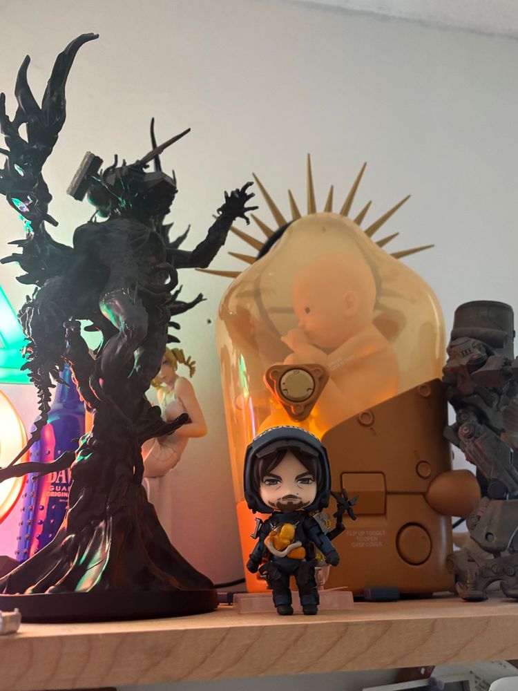 A photograph of a shelf filled with figurines, including but not limited to: The Magellan Man, Nendoroid Sam Bridges, 1:1 scale BB unit, Cherno Alpha, Catherine