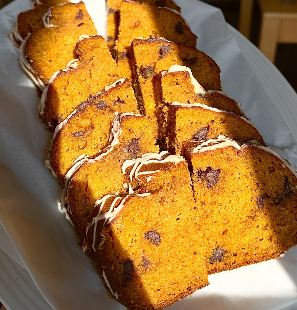 Sliced chocolate chip pumpkin bread on a sheet of parchment paper on a long platter. White icing drizzled over the top.