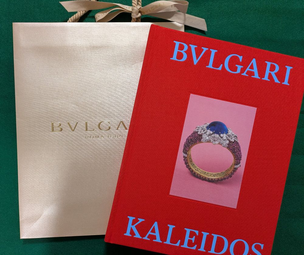 BVLGARIの紙袋と、ブルガリカレイドス展の図録。
紙袋は、持ち手のところにリボンが結んである。
図録は赤地にサファイアの指輪。