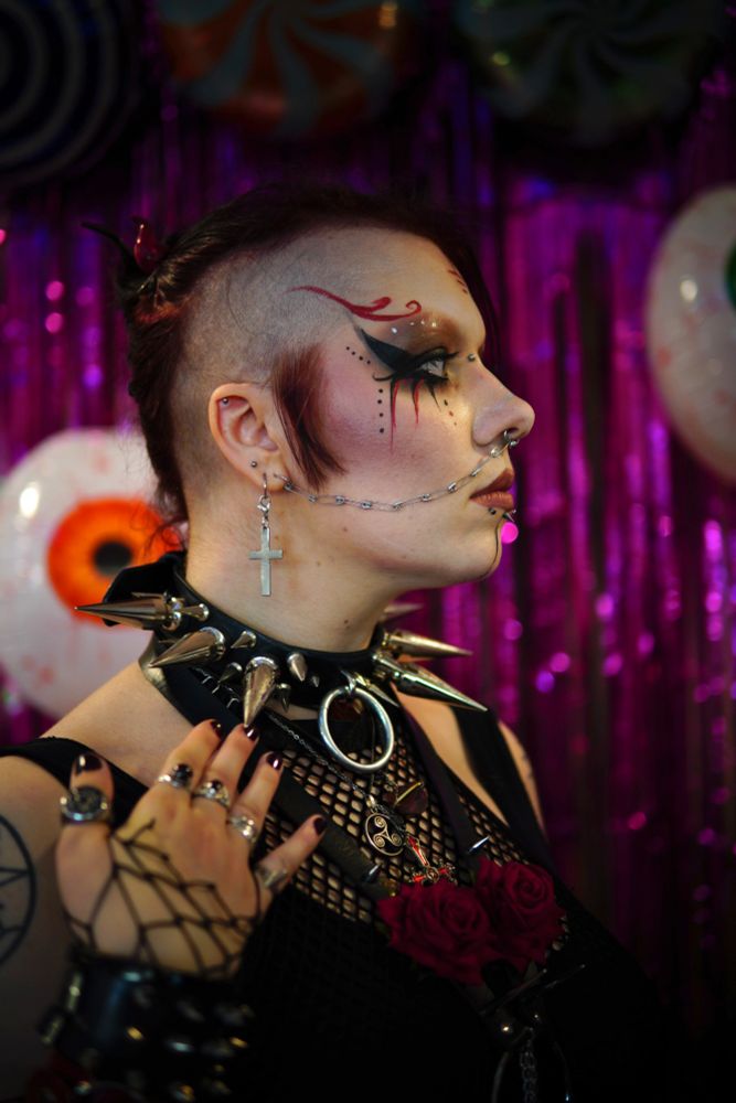 Goth women with tattoos and piercing, nose chain, side cut, heavy dark makeup, large choker