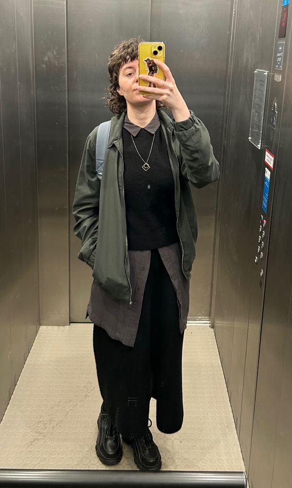 Bild von mir in einem Aufzugspiegel mit schwarzem Rock, schwarzen Buffalo Plateau Sneakern, einem langen grauen Hemd, darüber einem schwarzen Pullunder und einer grauen Jacke