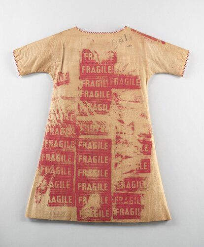 Textured white (faded to brown) paper with red and white striped binding; silk screened with magenta pattern of repeated text "FRAGILE"

A-line; above knee-length; short sleeves; wide scoop neck; inscribed with the word "DALI" (possibly)