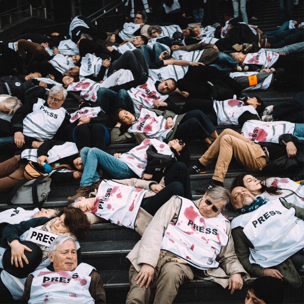 Des dizaines de journalistes allongés sur les marches, portant des chasubles « PRESS » tachées de faux sang, lors d’un die-in symbolique en hommage aux plus de 200 journalistes tués à Gaza.