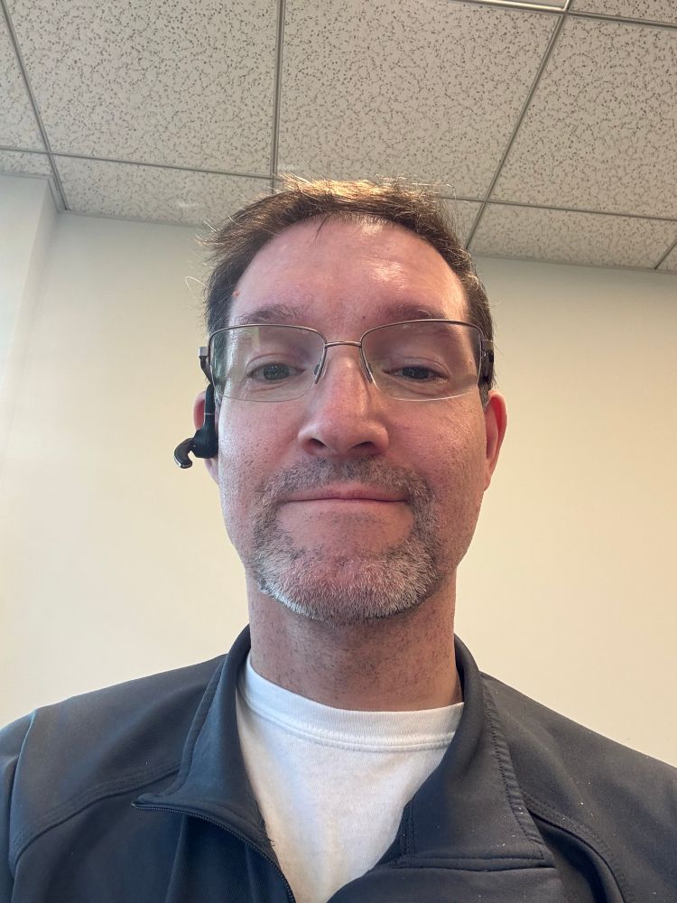 Work selfie wearing a wireless ear piece.