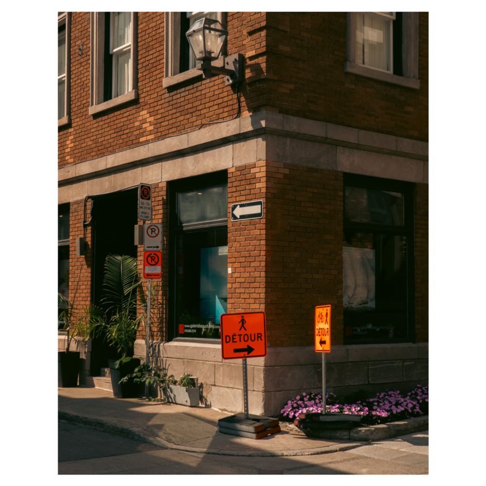 Un bâtiment en briques en ville, très contrasté, avec des panneaux détour sur le trottoir.