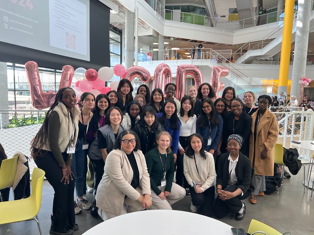 Smiling group photo of Kaylie — kneeling in front wearing a green sweater and khaki pants — with 25+ of diverse Women in Tech members at Harvard’s WeCode event