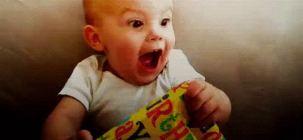 a baby is sitting on a couch holding a piece of birthday wrapping paper .