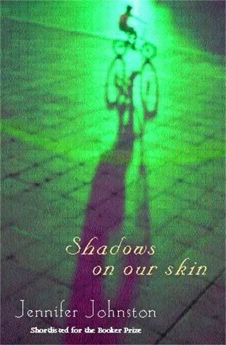 The front cover of the Jennifer Johnston book Shadows on Our Skin; it shows a blurred child on a bike at the top of the image, under a green light which casts over the whole image, and the child’s shadow reaches the bottom of the image. 