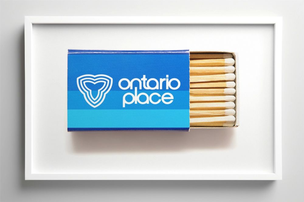 A framed image of a box of matches featuring the Ontario Place logo. The box is blue with a white logo and text reading 'Ontario Place' in lowercase letters. The match heads are visible on the right side of the partially open box.