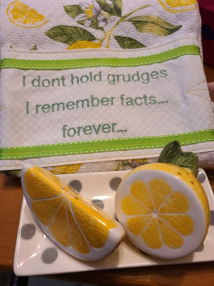 Lemon salt and pepper shakers on a polka-dot tray and a lemon themed kitchen towel with the text "I don't hold grudges. I remember facts... forever..."