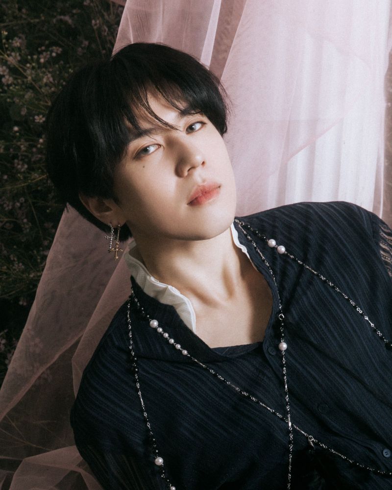 Not by the moon era Yugyeom. He's got dark short hair with bangs, a dark shirt with a white collar and a chain/pearl necklace/suspenders on top of it. He's got two earrings on his right ear and he looks ethereal.
