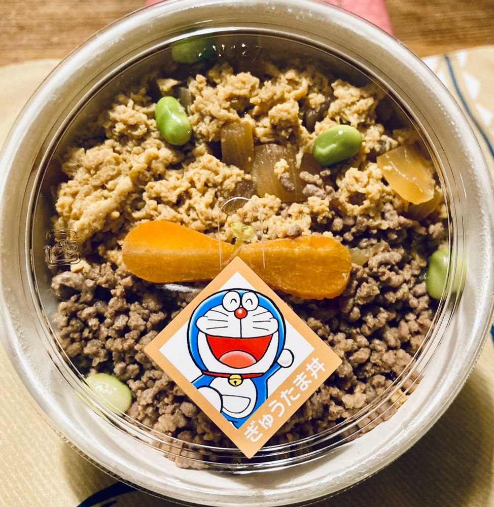 浅草今半のぎゅうたま丼。透明なフタの中央にドラえもんのシールが貼られており、中身のぎゅうたま丼の中央にはタケコプターをイメージしたニンジンが載っている。
