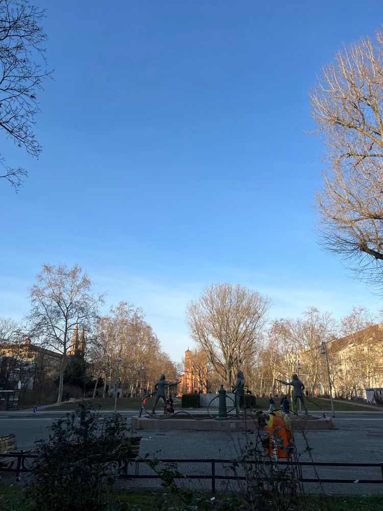 a photo of mariannenplatz with the sun shining on saint thomas church and blue skies