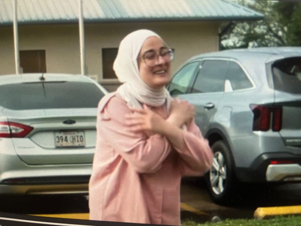Rümeysa Öztürk, smiling with arms crossed, walks through a parking lot.