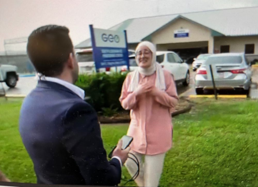 Rümeysa Öztürk, smiling, greets a reporter on grass surrounding a parking lot.