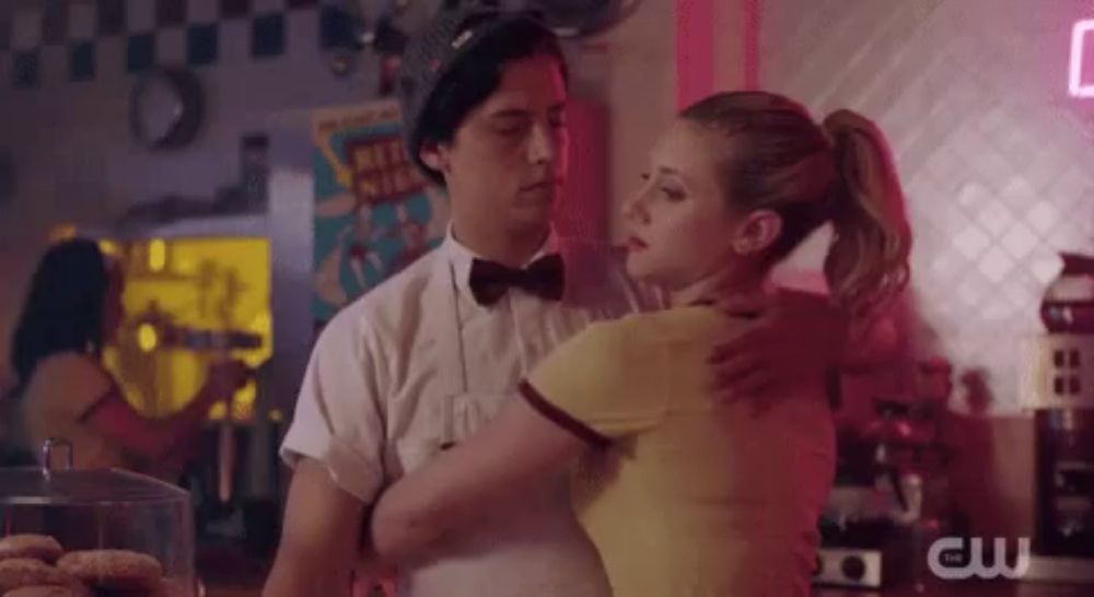 a man and a woman are dancing in a diner . the woman is wearing a yellow shirt .