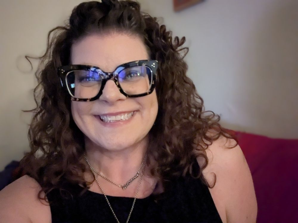 Middle-added white woman with dark, curly hair, tortoise shell glasses, and a black top.