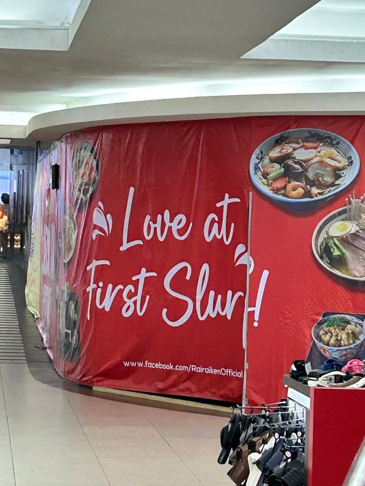 A poorly thought out advertisement for ramen shop. The sign says "love at first slurp" but the angle of it as it wraps around the architecture it's plastered on makes it look like it reads "love at first slur"