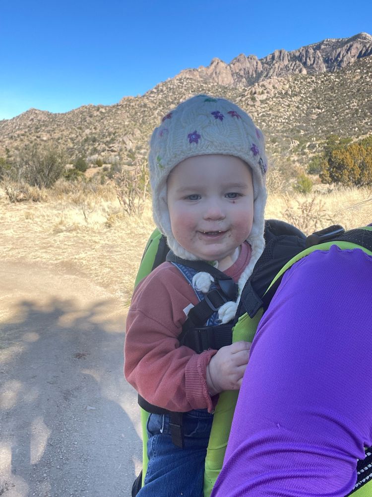 Baby in carrier on trail smiling at camera 