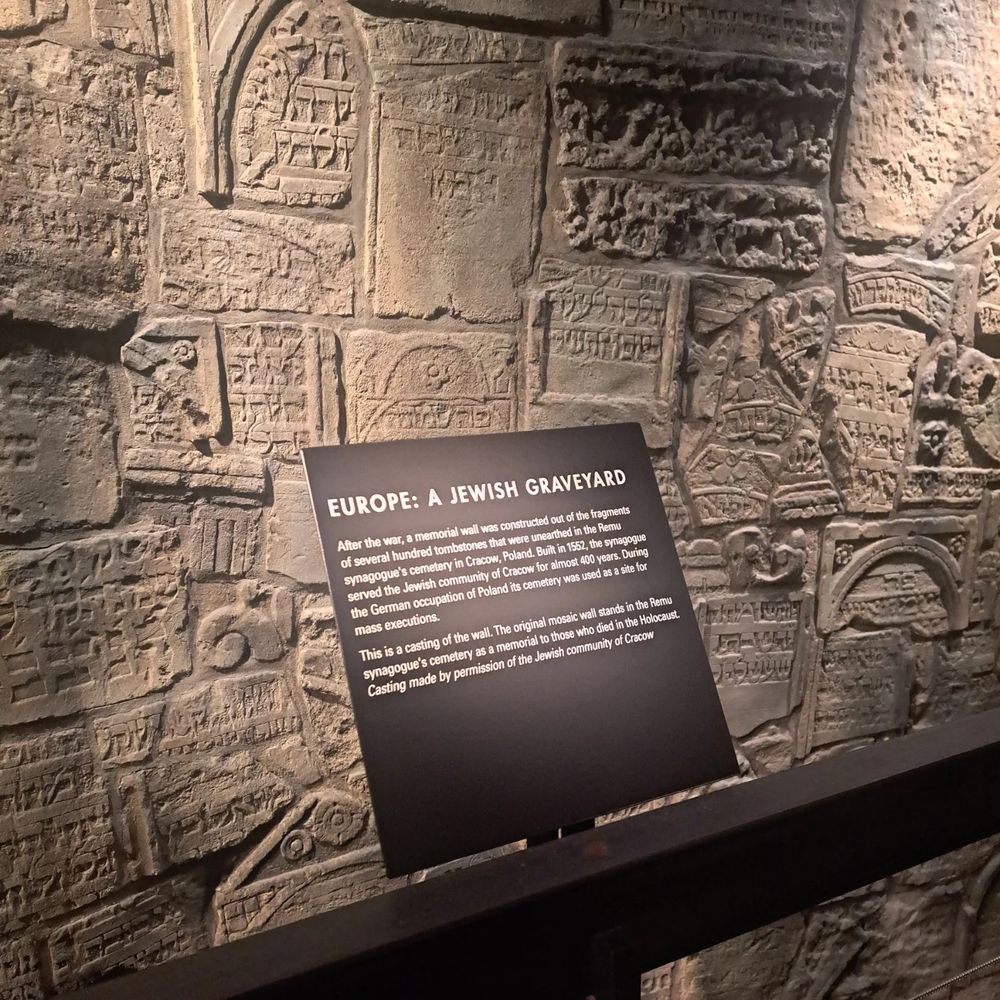 This is a wall replicating gravestones of Jewish people who died in the Holocaust with a placard that says Europe is a Jewish graveyard.