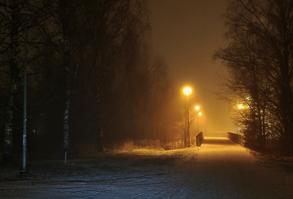 A photo of orange streelights and a small bridge. The ground is lightly covered in snow.