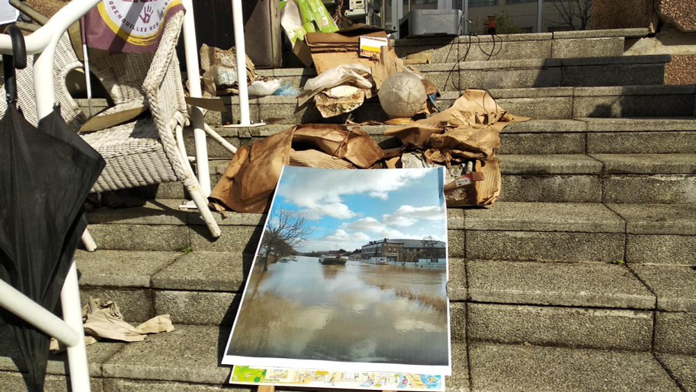 Sur les marches du siège Axa de Nantes, des déchets issus des inondations récentes à Redon accompagnés d'une photo de ces inondations