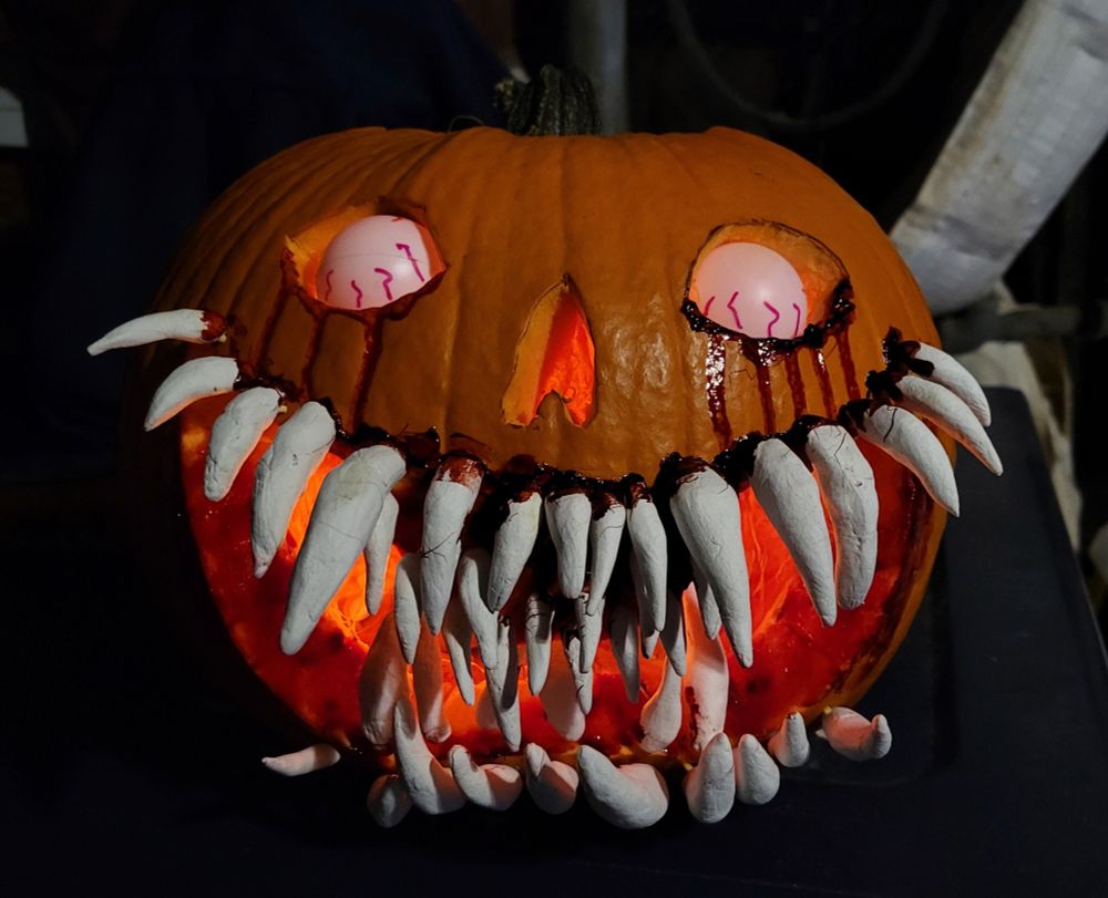 Jack o lantern with rolled up eyes and many layers of teeth made out of white clay. Fake blood is all over its mouth.