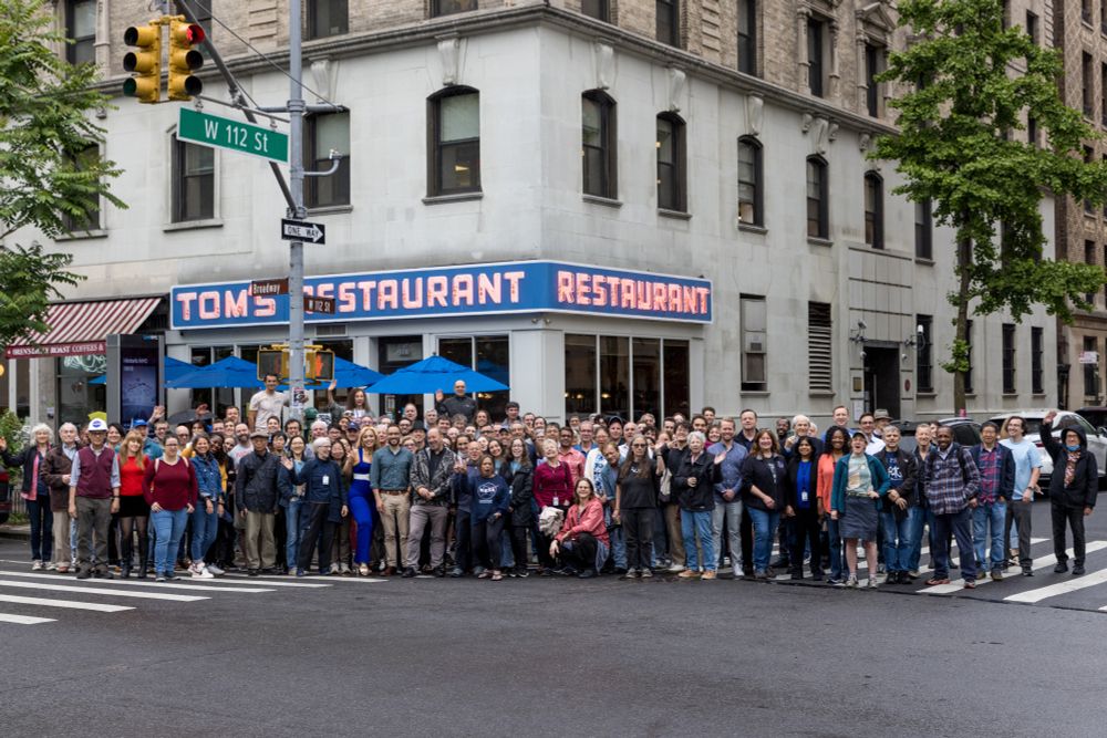 Photo of the a large group of GISS employees/colleagues in front of Toms Restaurant with a prominent street sign saying "112th St" taken from the middle of Broadway. Credit: Tricia Baron.
