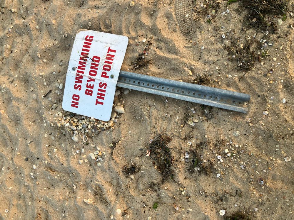 A fallen sign in the sand saying “no swimming beyond this point”