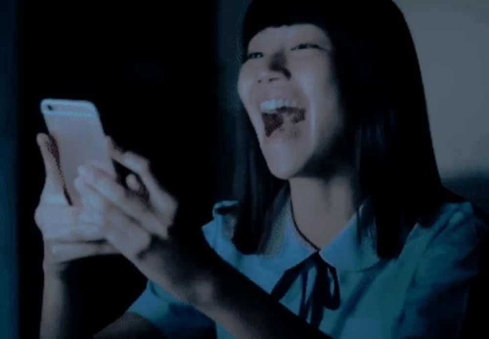 a girl is laughing while looking at a cell phone