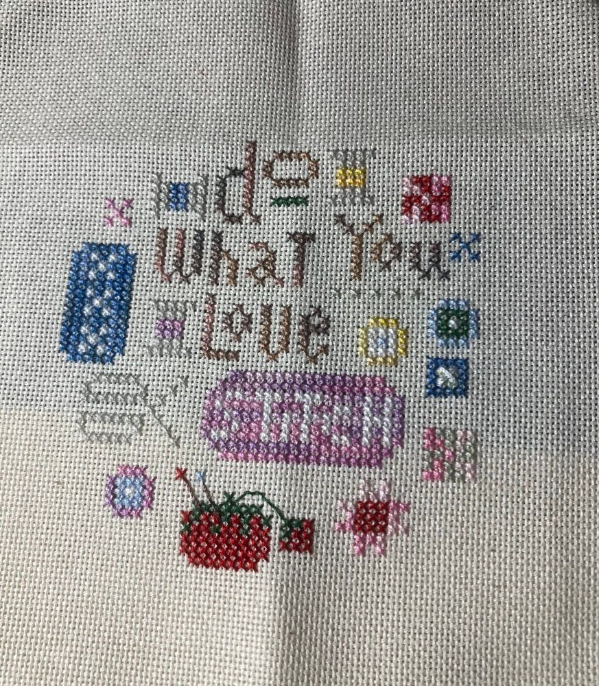 A cross stitch piece. Says “Do What You Love—Stitch “.