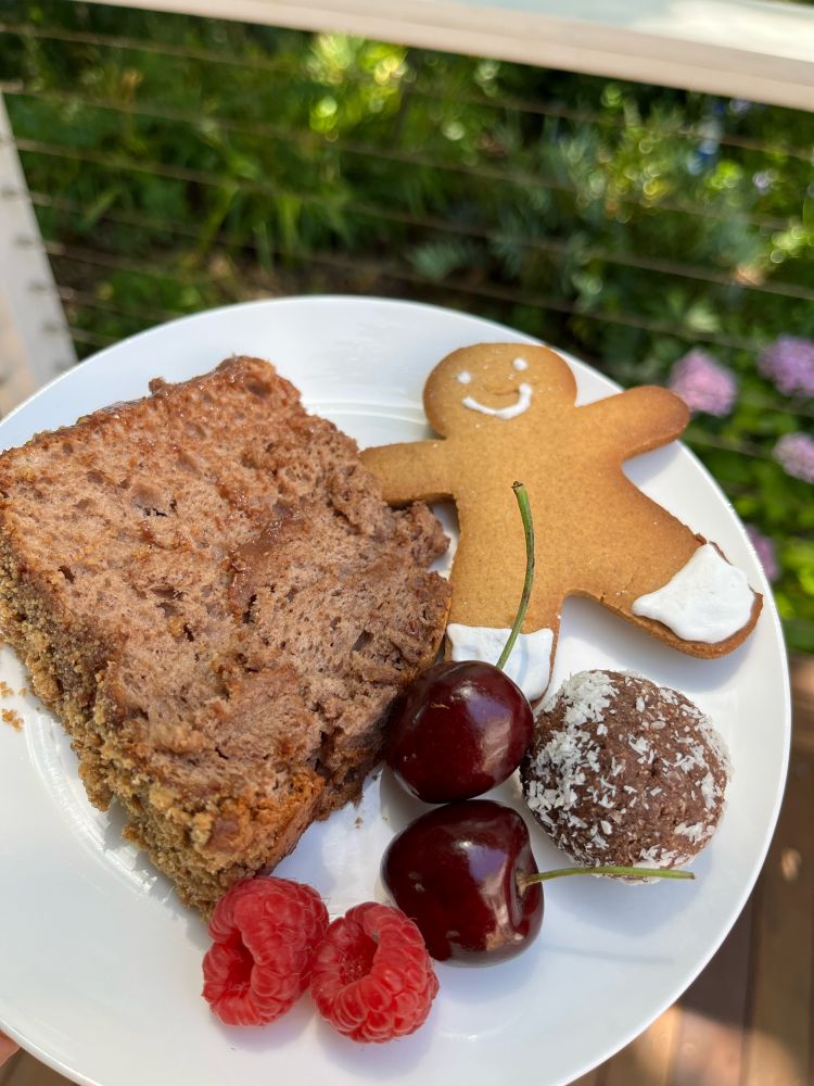A plate with a slice of cake, a gingerbread man, a rumball, cherries and raspberries 