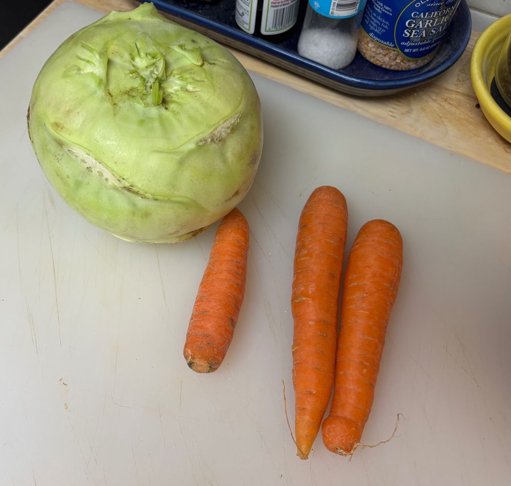 A large kohlrabi and three carrots sit on a cutting board.