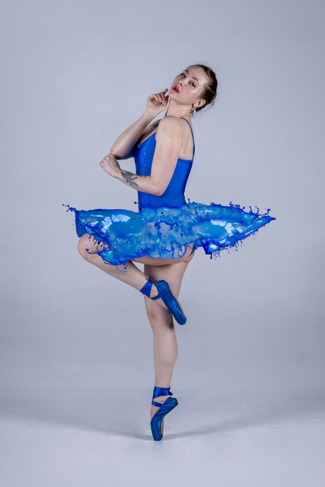A dancer / model stands on pointe in blue ballet shoes. Wearing a royal blue tu-tu where the skirt has been replaced to look like it's made of water splashes instead of fabric.