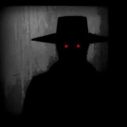 The Benadryl hat man, a dark figure in all black with red eyes staring at the camera 