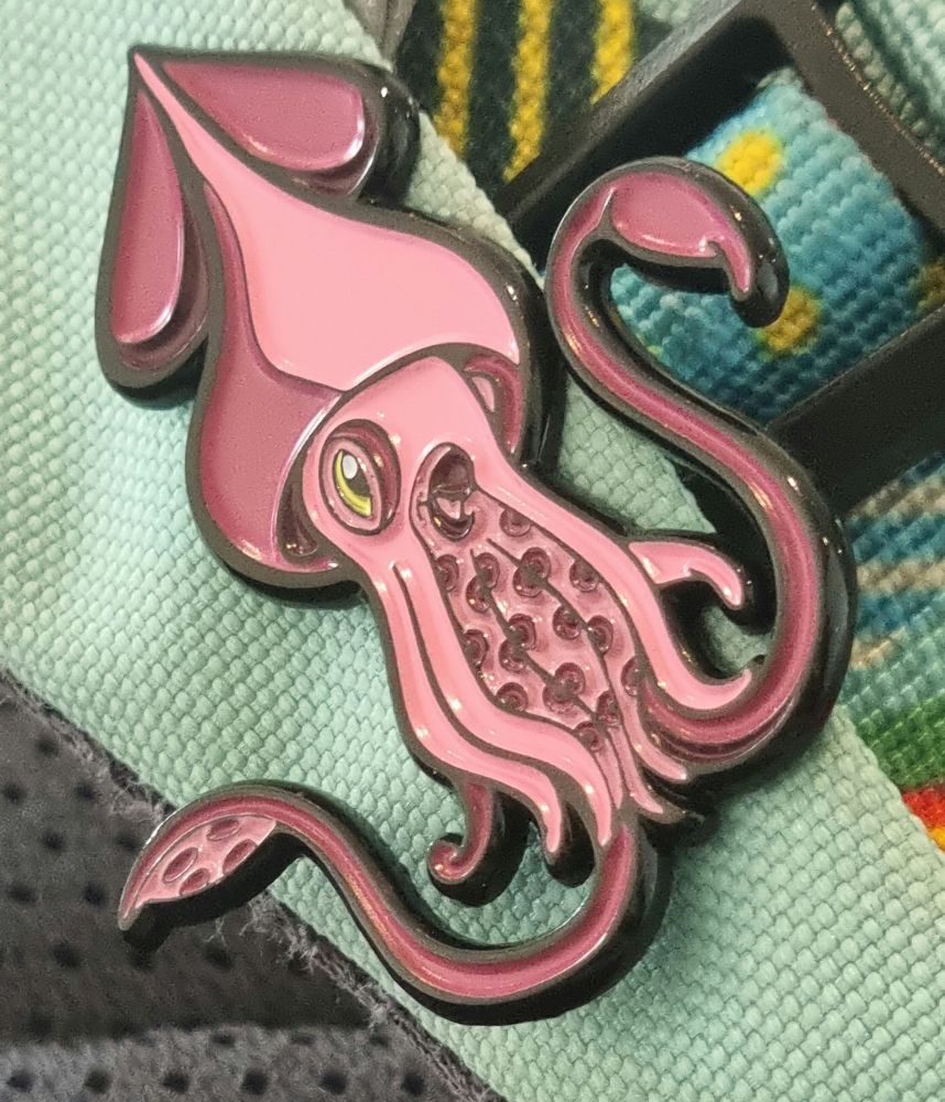 An enamel pin of a Colossal squid attached to a blue bag 