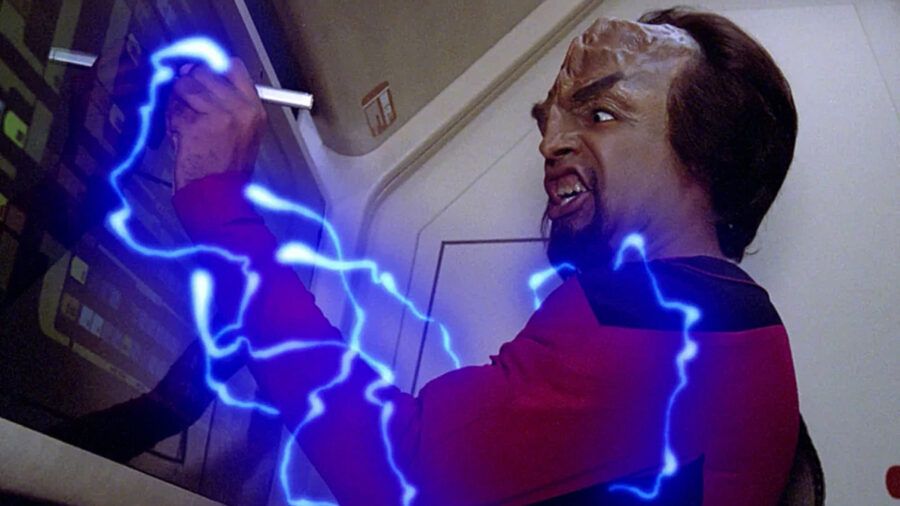 Worf in a red Starfleet uniform at a computer console onboard the Enterprise. Blue electricity is coursing through his body and Worf's face is grimacing in agony.