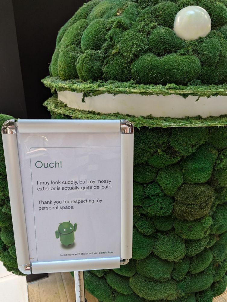 Zoom into the sign next to the Android mascot made out of moss. Sign reads: Ouch! I may look cuddly, but my mossy exterior is actually quite delicate. Thank you for respecting my personal space.