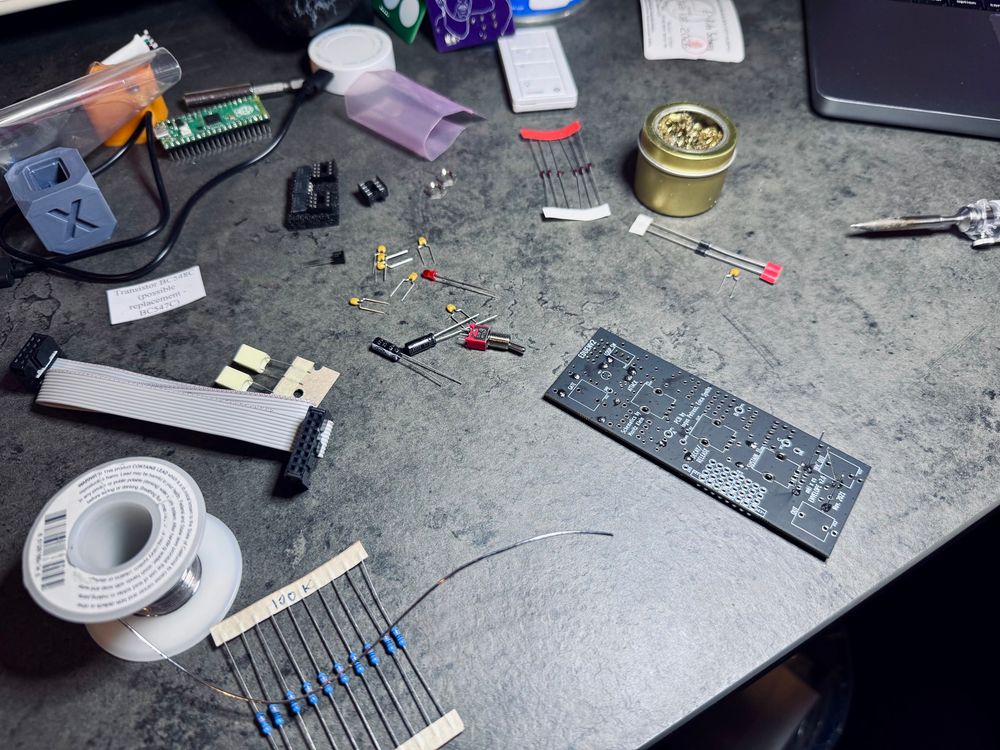 Partially assembled EG synth module with electronics components, solder, and a soldering iron on the desk
