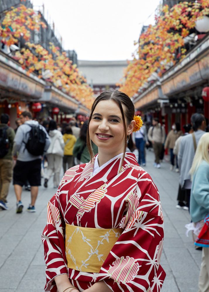 Young lady in red and white kimono. Hair in a bun with colorful flowers. Standing at the entrance of Asakusa, Japan. 
