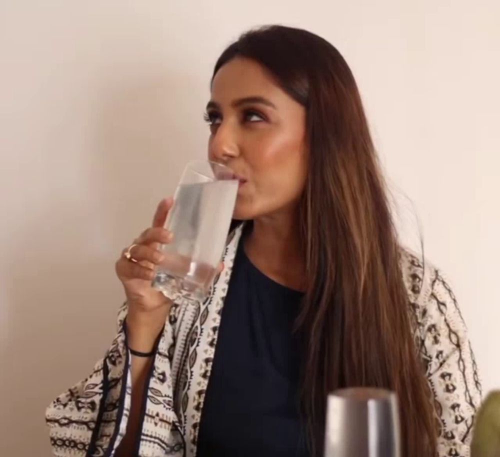 a woman drinking a glass of water while wearing a black shirt