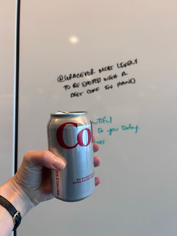 Image of me holding a Diet Coke… in the background there is written in a whiteboard a superlative “@gracevor most likely to be spotted with a Diet Coke in hand” 